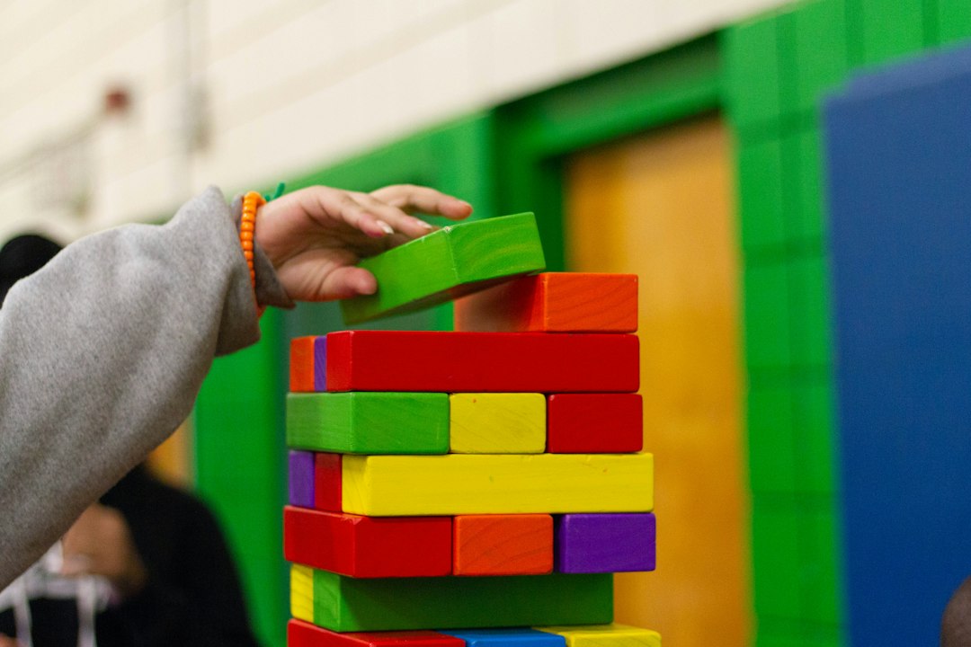 Mano colocando un bloque verde sobre una construcción de bloques de madera de distintos colores.